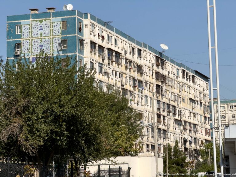 Weathered apartment block with enclosed balconies, satellite dishes, and decorative upper-wall panels.