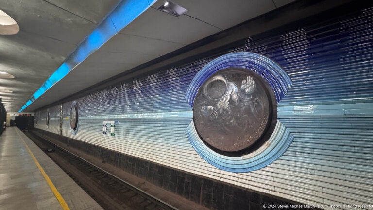 Blue-tiled Kosmonavtlar platform wall with a large round cosmonaut and planet relief.