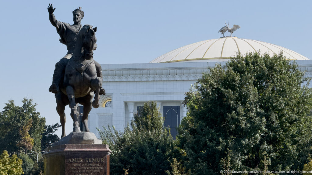 Amir Timur equestrian statue before a white domed building crowned by bird sculptures.