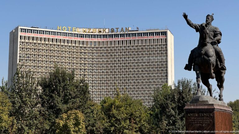 Hotel Uzbekistan behind the raised rider and horse of the Amir Timur Monument above trees.
