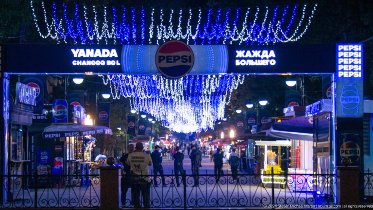 Festival or entertainment entrance covered with blue lights and food signs at night.