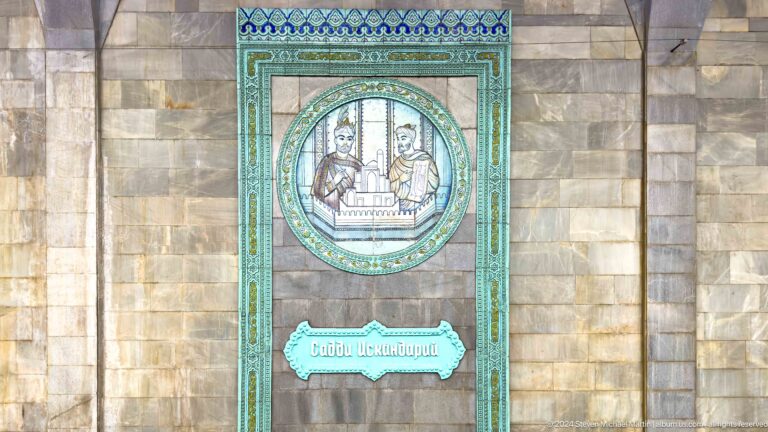 Turquoise framed tile panel of two scholars holding an architectural model above a Cyrillic plaque.