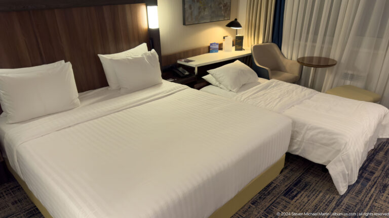 Hotel room with a double bed, single bed, desk, chair, bedside lights, and closed curtains.