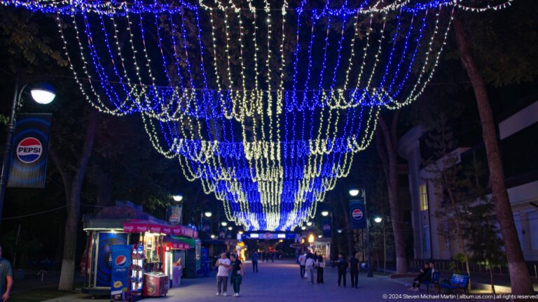 People walking beneath a canopy of blue and white decorative lights.