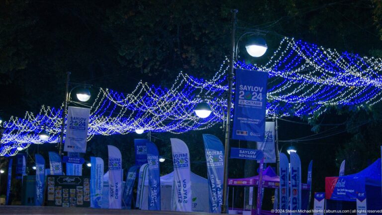 Outdoor seating beneath blue string lights and hanging banners at night.