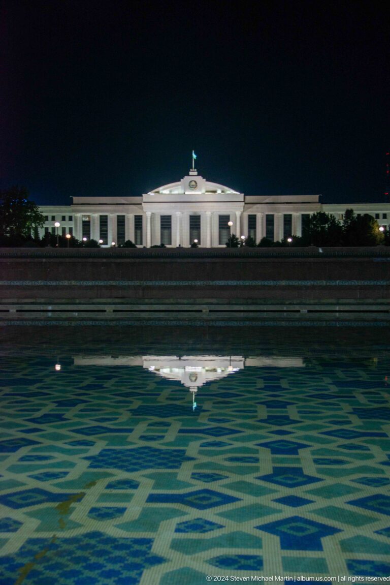White colonnaded building reflected in a dark fountain pool.