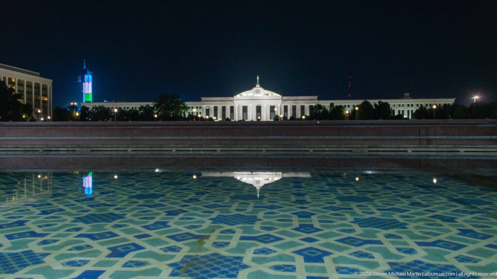 Patterned fountain basin leading toward a white pavilion at night.