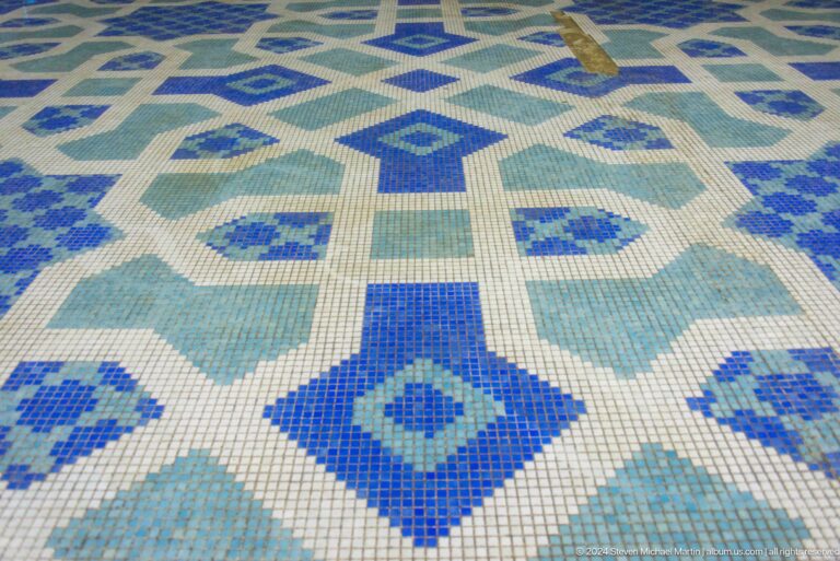 Close view of blue, green, and cream geometric mosaic pavement.