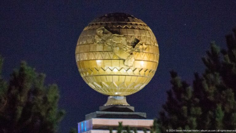 Golden globe monument with raised map relief and patterned bands illuminated at night.