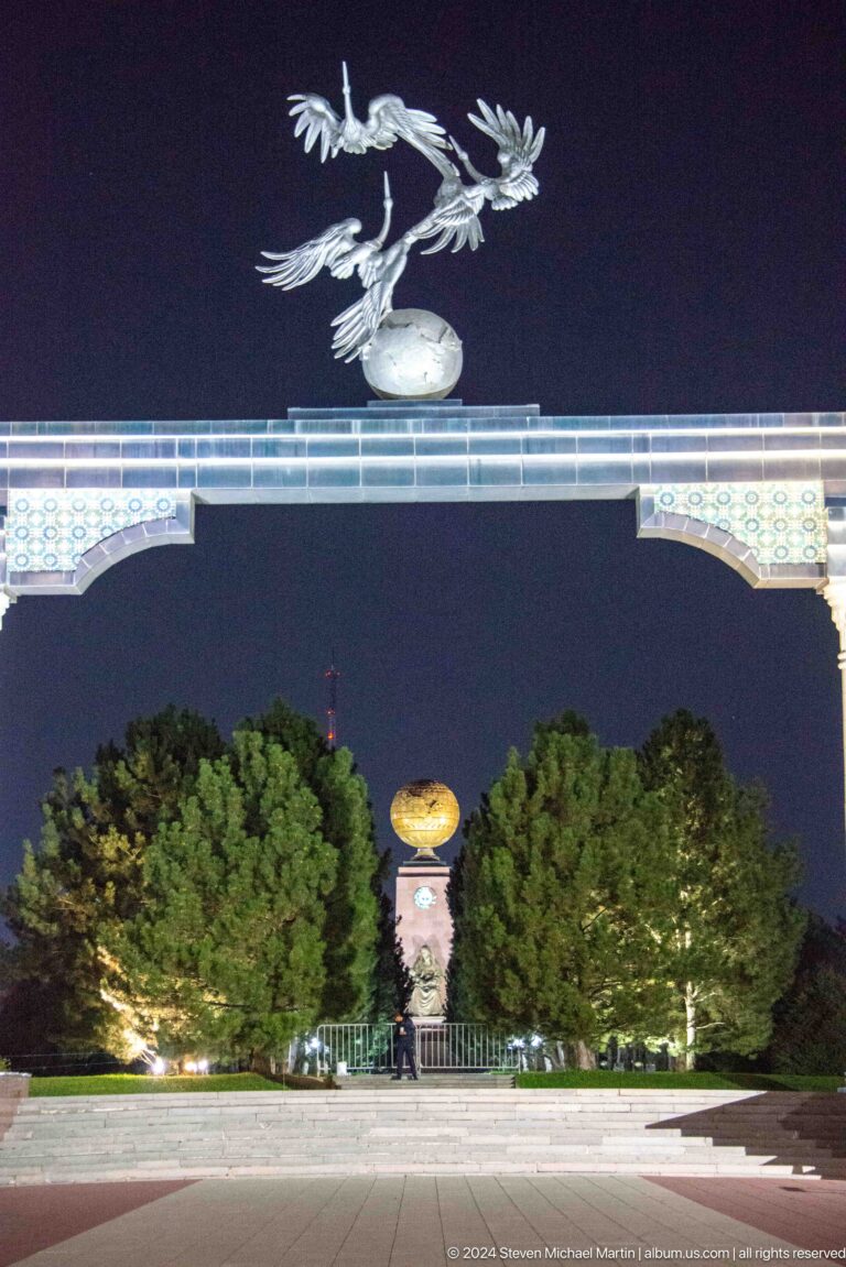 Decorated monumental arch framing a distant golden globe between tall trees at night.