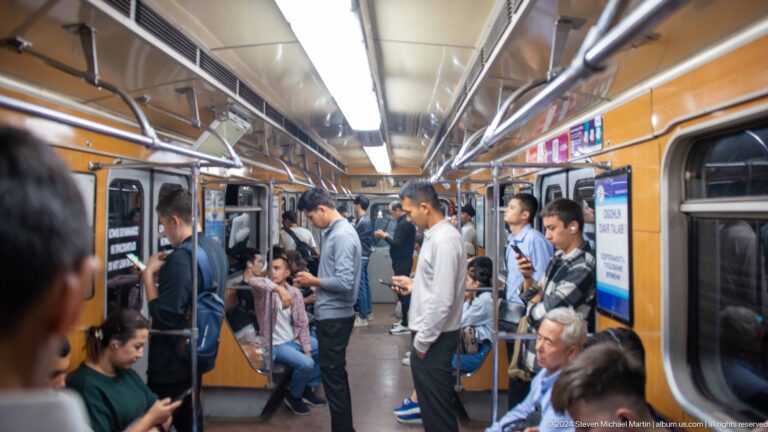 Passengers standing and sitting inside an orange-trimmed Tashkent Metro carriage.