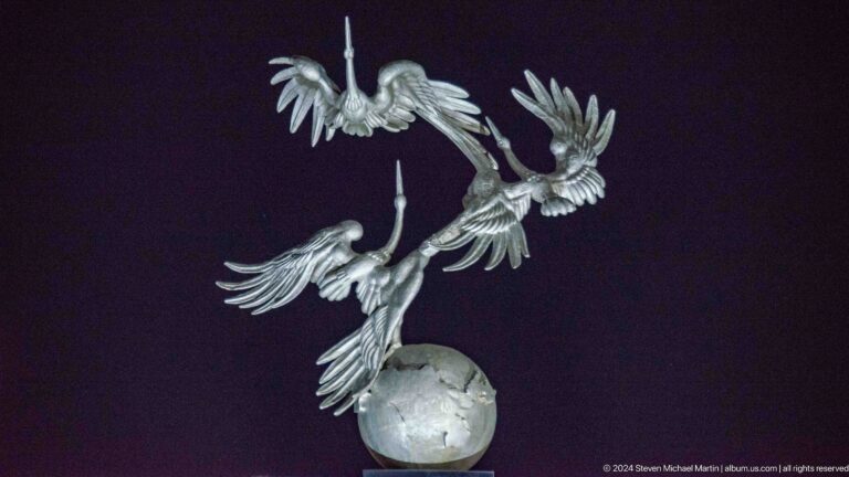 Close night view of three silver storks spiraling upward above a globe.