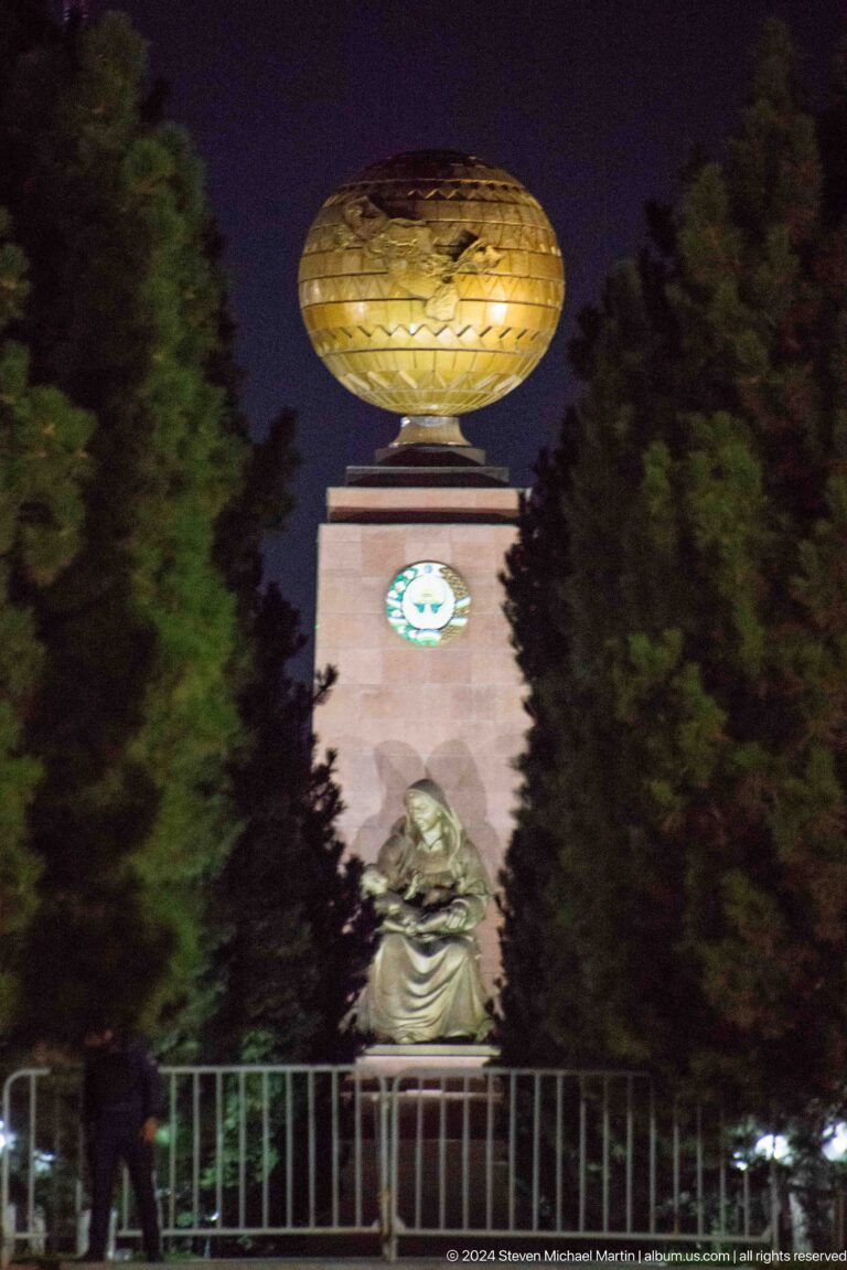 Seated grieving woman below a tall stone monument with a state emblem and golden globe.