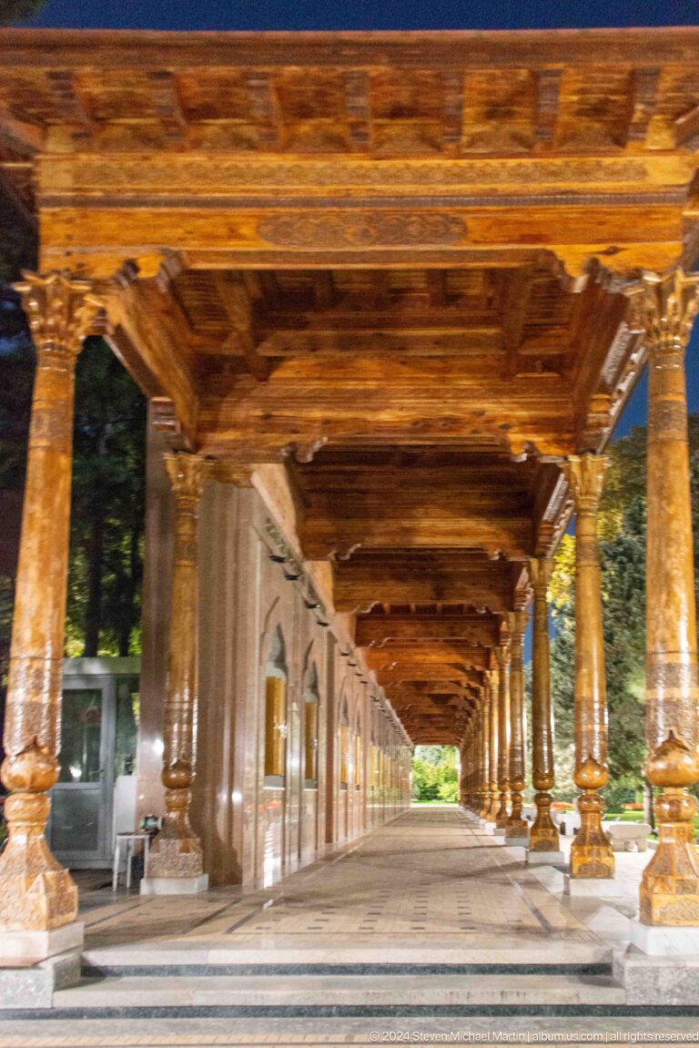 Long covered memorial passage with carved wooden columns and a coffered timber ceiling.