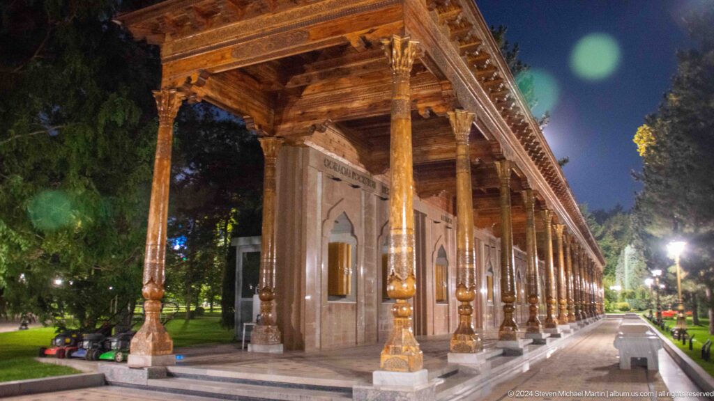 Carved wooden portico beside a pale stone memorial wall with pointed-arch golden panels.