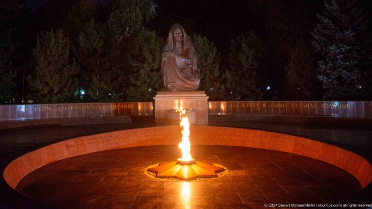 Eternal flame burning before a seated bronze grieving woman in a circular memorial court.