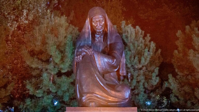 Close view of a hooded bronze woman seated with bowed head and hands together.