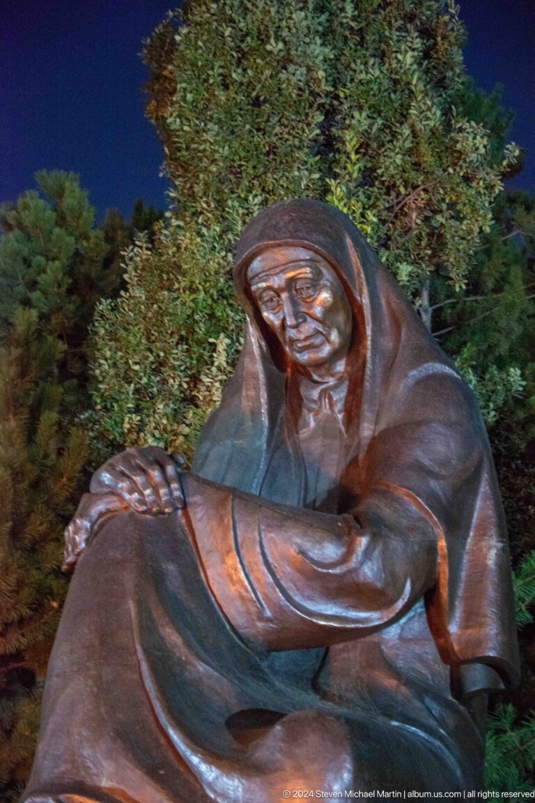 Close view of a hooded bronze grieving woman with her hands resting on one knee.