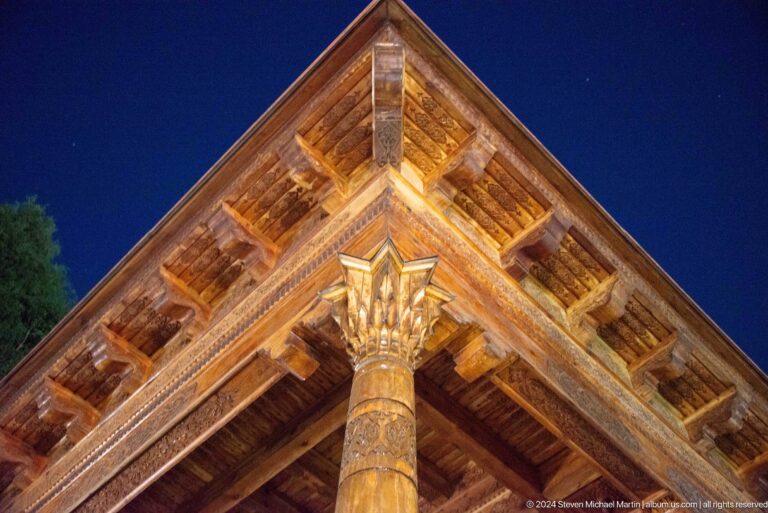 Upward view of a carved wooden roof corner and ornate column capital.