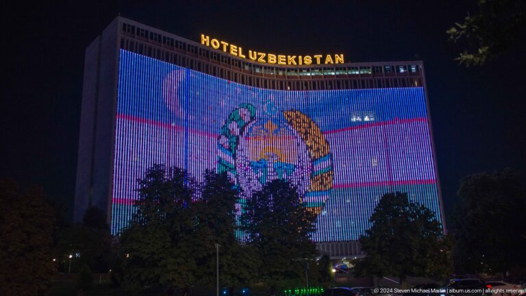 Hotel Uzbekistan illuminated with blue vertical lights and a large animated facade display at night.