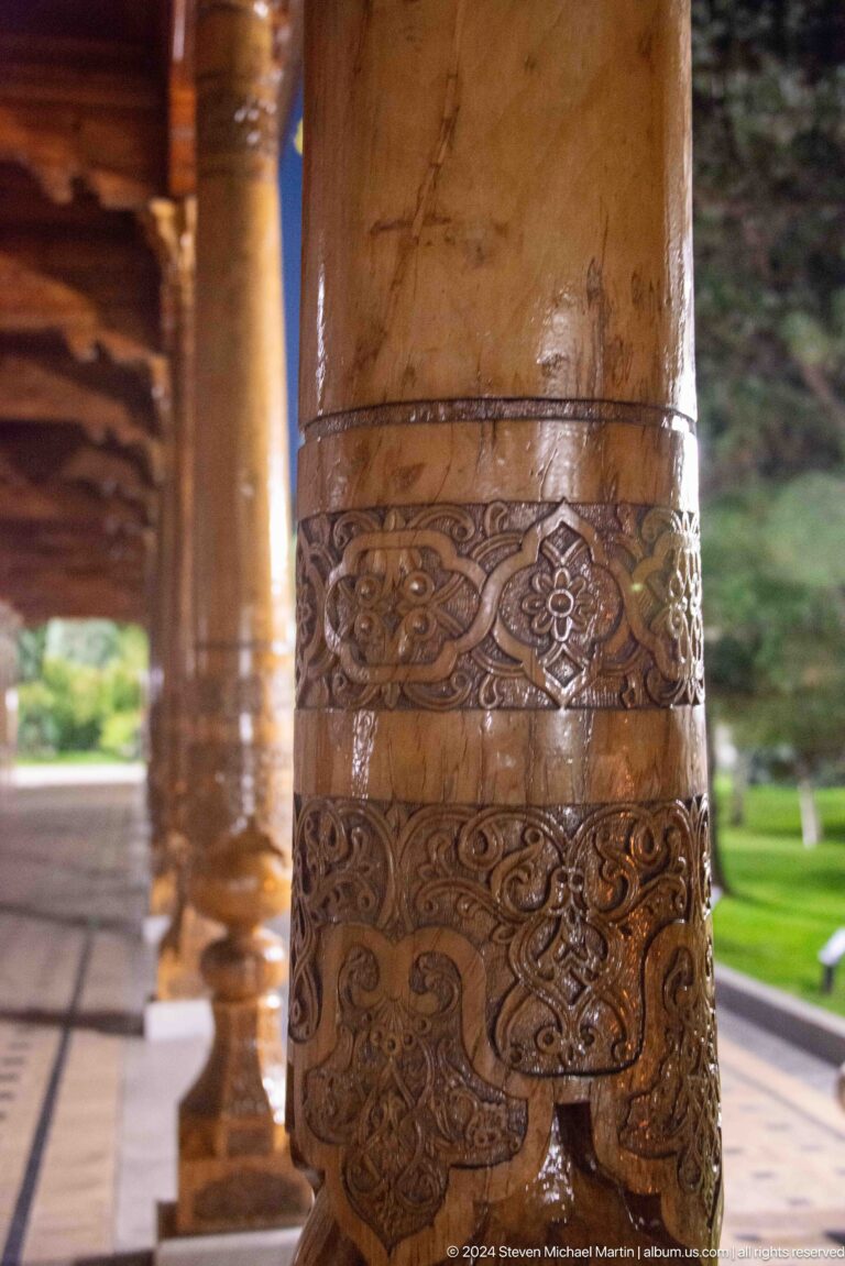 Close view of floral and scrolling relief bands carved around a polished wooden column.