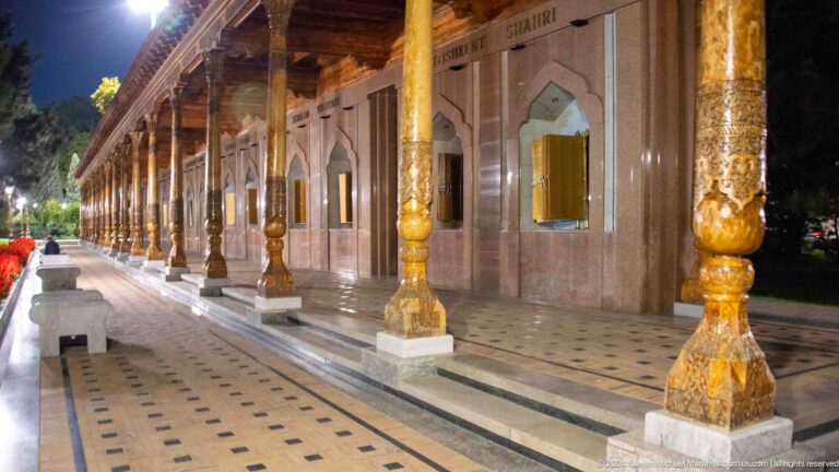 Long memorial gallery with carved wooden columns and golden books displayed in pointed-arch niches.