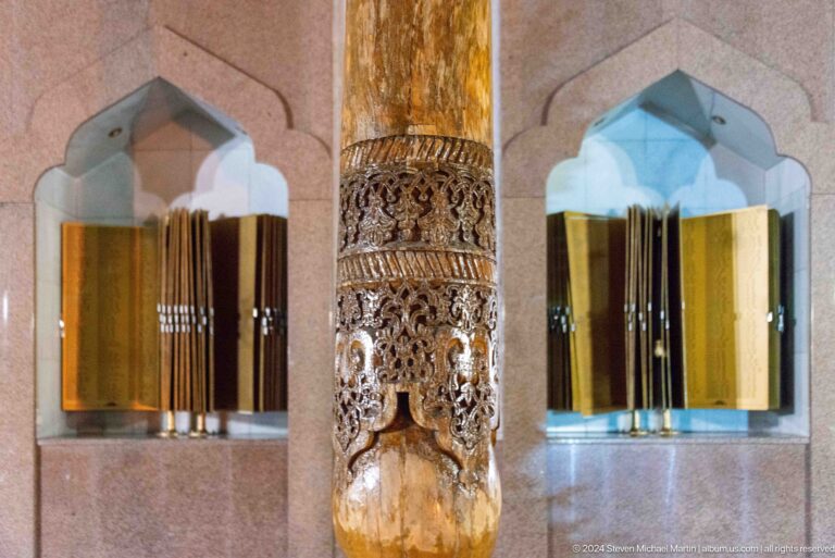 Carved wooden column beside golden memorial books displayed in pale stone niches.