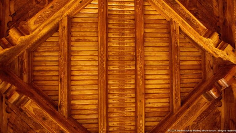 Upward view of closely spaced wooden roof slats meeting heavy timber beams.