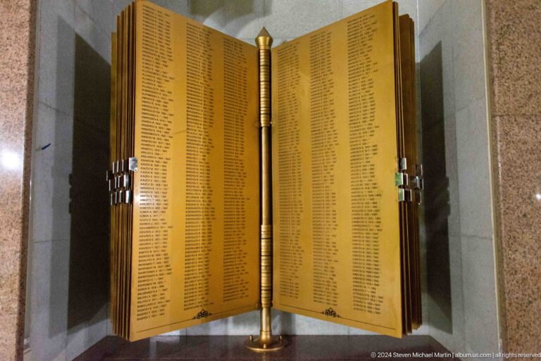 Golden open memorial book filled with columns of names inside a pointed-arch niche.