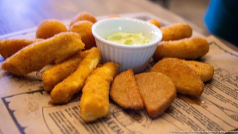 Basket of golden fried appetizers and croquettes arranged around a bowl of dipping sauce.