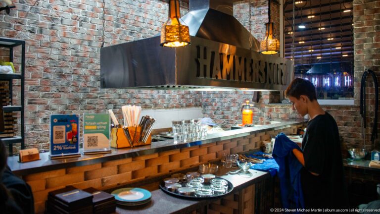 Modern Hammersmith restaurant counter with exposed brick, pendant lamps, and illuminated signage.