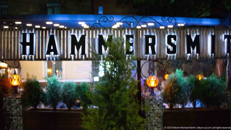Illuminated HAMMERSMITH letters across a dark restaurant facade behind trees at night.