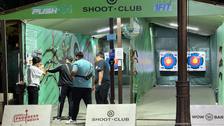 Visitors standing at the counter of an indoor shooting club with target graphics on the walls.