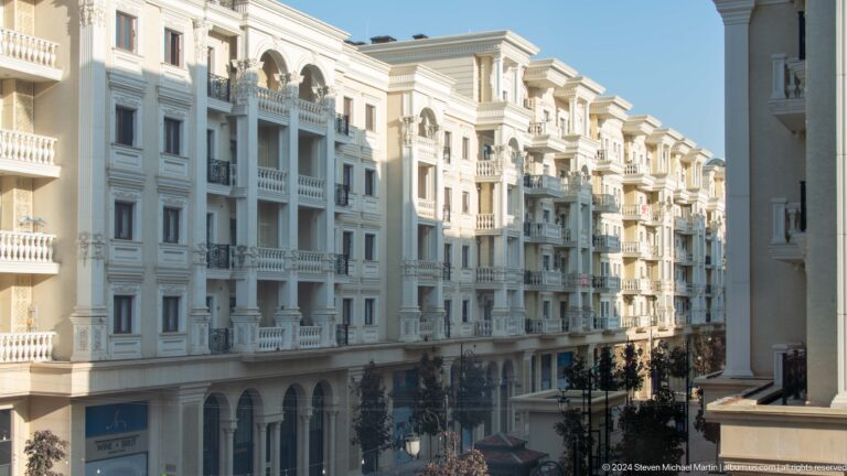 White apartment buildings with ornate balconies, arched windows, and classical columns along a Tashkent street.