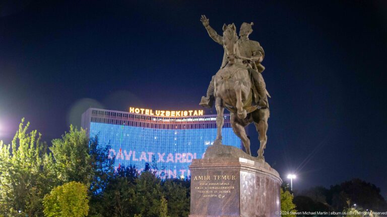 Amir Timur equestrian monument on its pedestal with illuminated Hotel Uzbekistan behind.