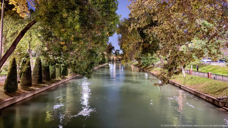 Tree-lined canal with clipped hedges, small fountains, and daylight reflections in Tashkent.