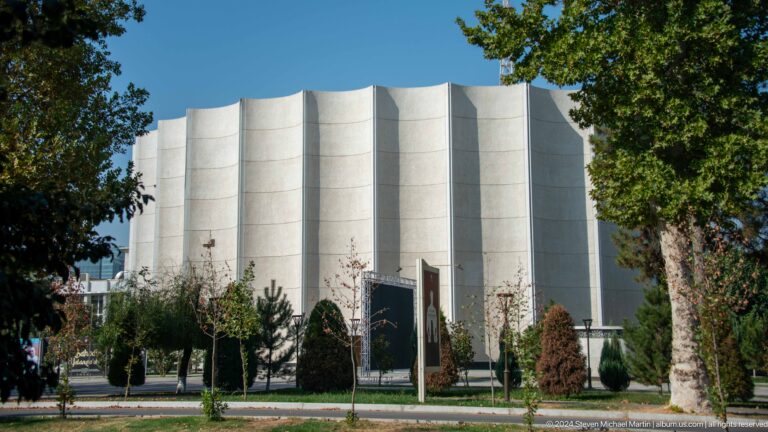 Large white civic building with tall curved vertical facade bays and a landscaped forecourt.
