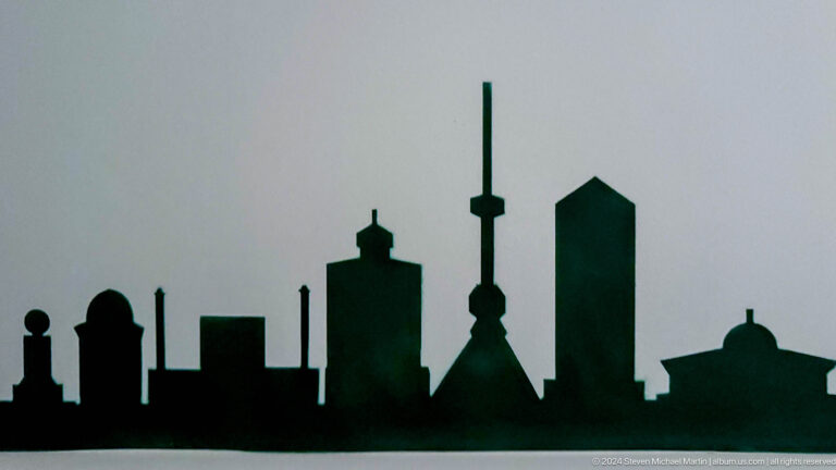 Black silhouette of towers, domes, and high-rises against a pale background.