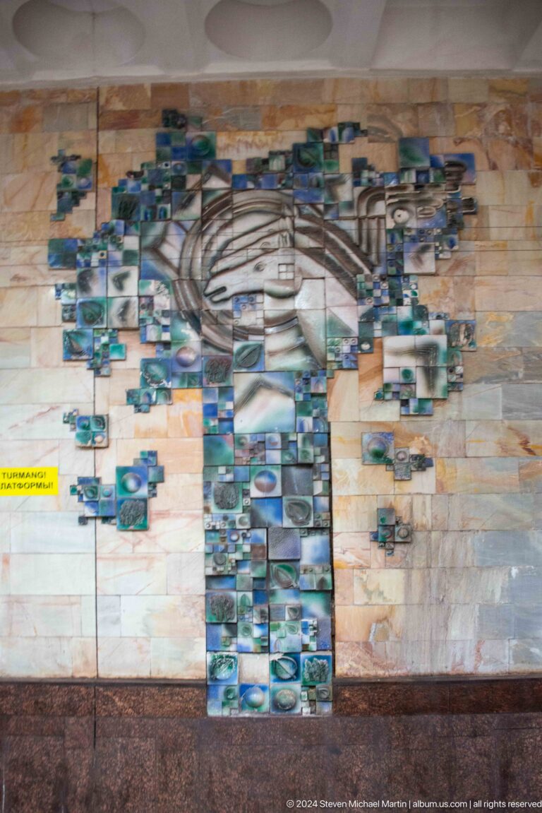 Large blue-green tile mosaic portrait on a pale wall at Kosmonavtlar Metro station.
