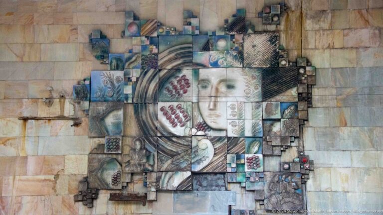 Large station mosaic of a woman's face surrounded by grapes, small figures, and irregular tile blocks.