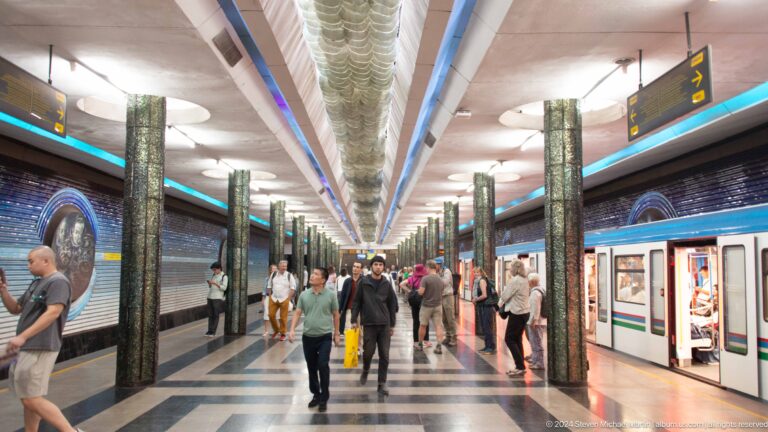 Passengers on a Kosmonavtlar Metro platform beside a white train with colored stripes.