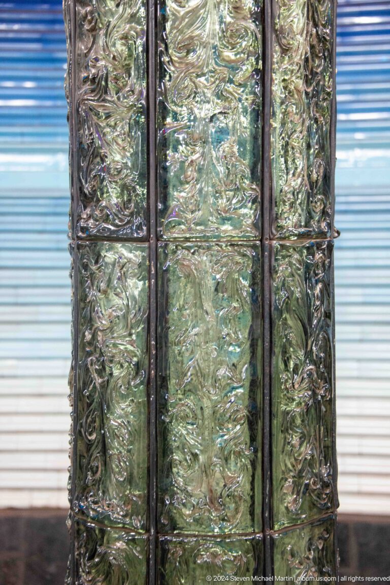Close-up of glossy green relief tiles covering a metro station column.
