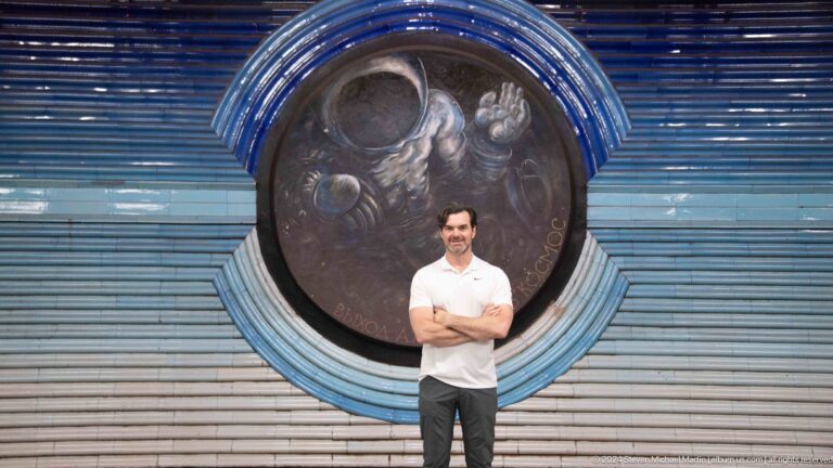 Adult male visitor with folded arms standing before a large circular cosmonaut relief.