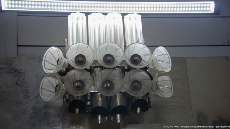 Cluster of white horn speakers, circular reflectors, and metal tubes mounted overhead.