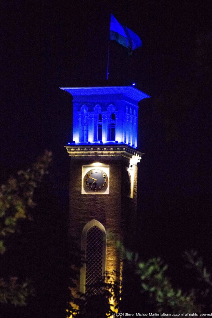 Blue-lit square clock tower with a round clock face against the night sky.