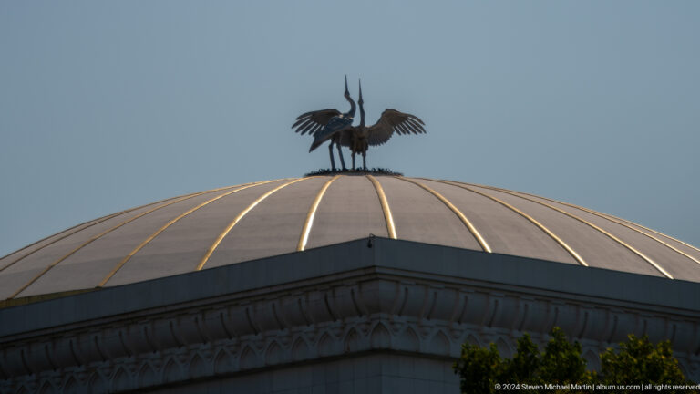 Bronze stork-like birds with spread wings standing atop a ribbed domed roof.