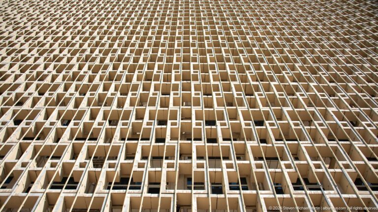Steep upward view of Hotel Uzbekistan's repeating concrete window screen.