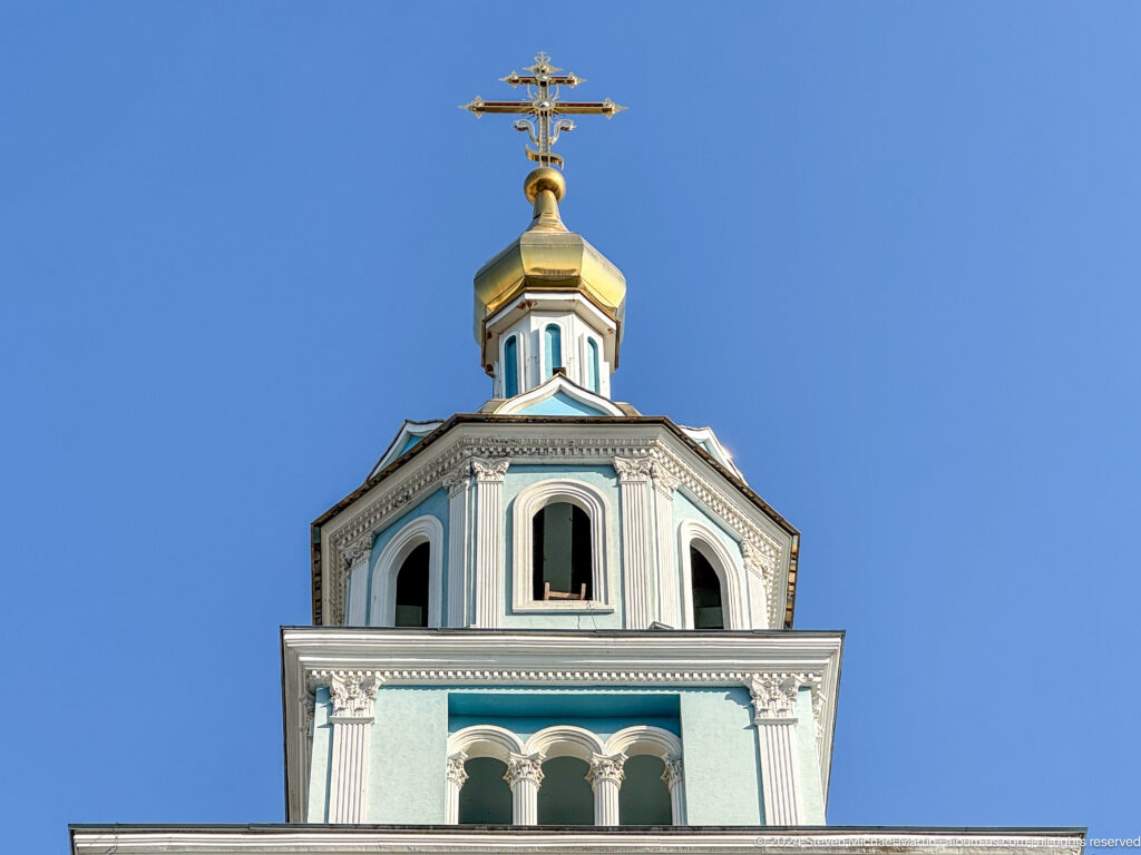 Upper octagonal bell tower stage with arched openings, gilded cap, and Orthodox cross.