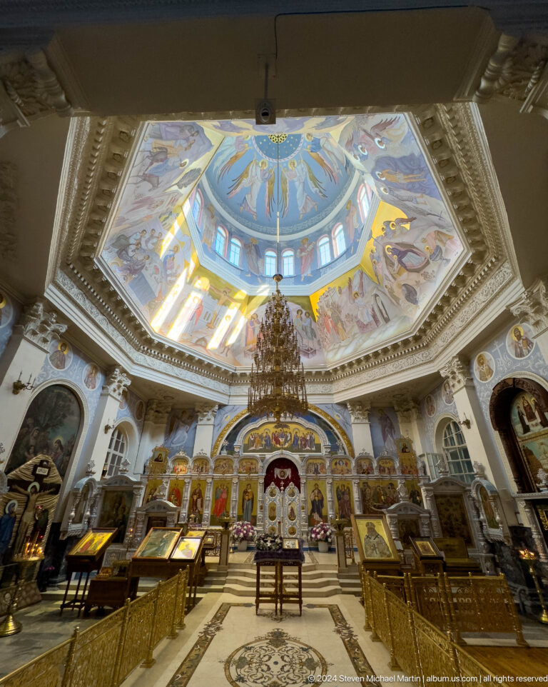 Wide cathedral interior showing painted dome, chandelier, and gilded iconostasis.
