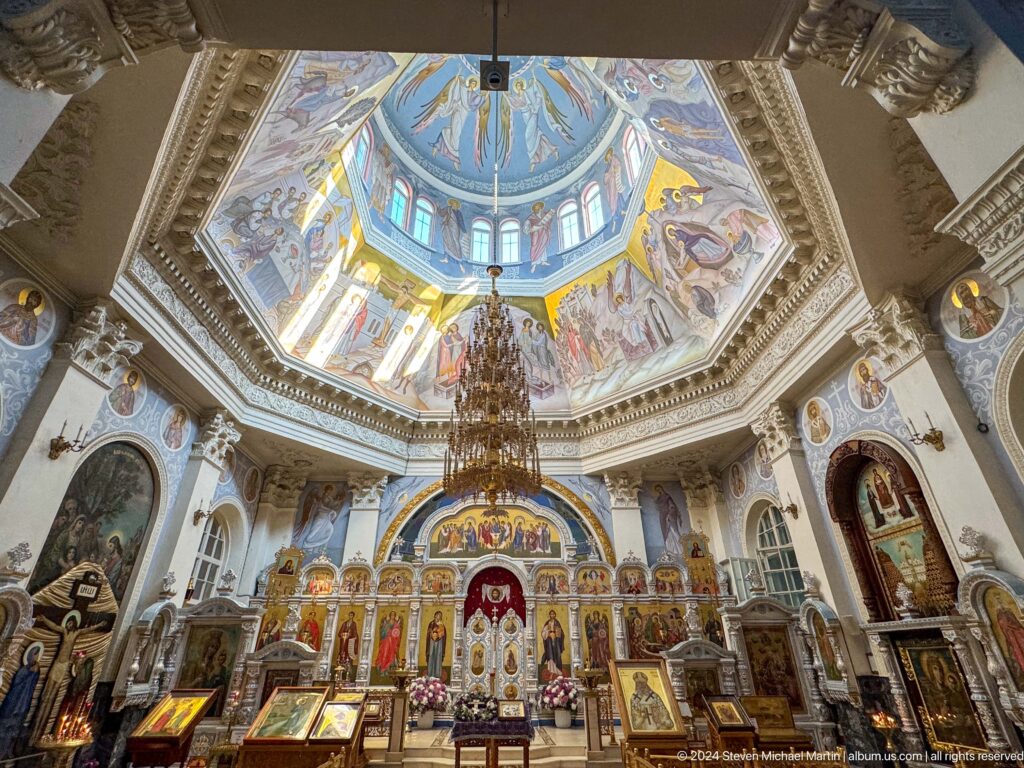 Symmetrical cathedral nave with painted dome, chandelier, gilded iconostasis, and marble floor.